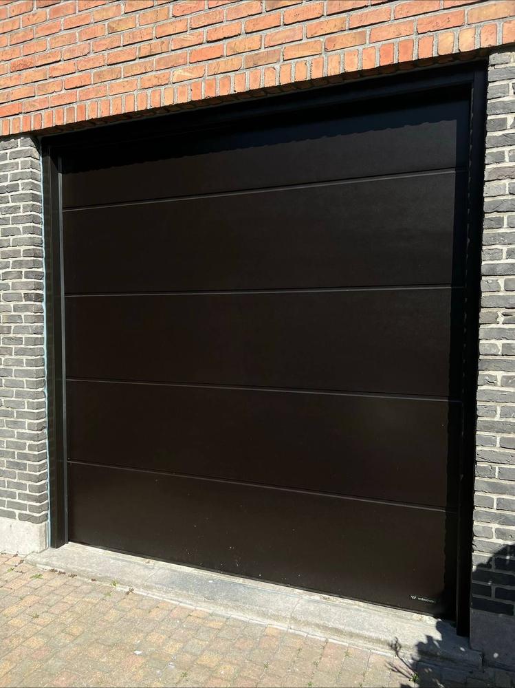 Porte de garage sectionnelle brun foncé posée en façade brique