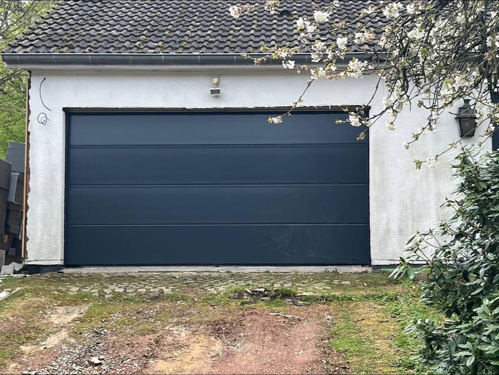 Porte de garage sectionnelle grise posée en façade pierre